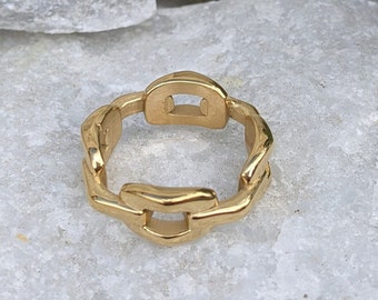 May include: A gold-toned ring with a chain-link design. The ring is made of a thick, chunky metal and has a simple, modern style.