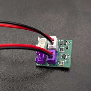 May include: A small green circuit board with two purple connectors and two white connectors. Red and black wires are connected to the connectors.