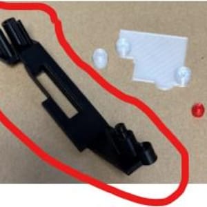 May include: A black plastic part with multiple holes and a slot in the center. It is a 3D printed part with a white and red plastic piece.