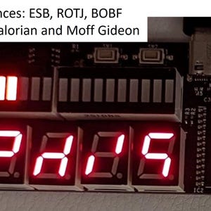 Op de afbeelding: Een zwarte elektronische printplaat met een rij van vijf rode zeven-segment LED-displays die de tekst E2A15 tonen, twee LED-balkgrafieken waarvan er één verlicht is, en tekst: 6 sequences: ESB, ROTJ, BOBF 2xMandalorian and Moff Gideon.