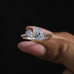 May include: A silver ring with two pear-shaped diamonds. The larger diamond is on the top and the smaller diamond is on the side.