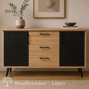 Puede incluir: Un aparador rectangular con acabado de veta de madera clara, tres cajones centrales y dos armarios laterales. Las puertas tienen una textura acanalada vertical en negro. El mueble se apoya sobre cuatro patas negras cónicas con tiradores negros.