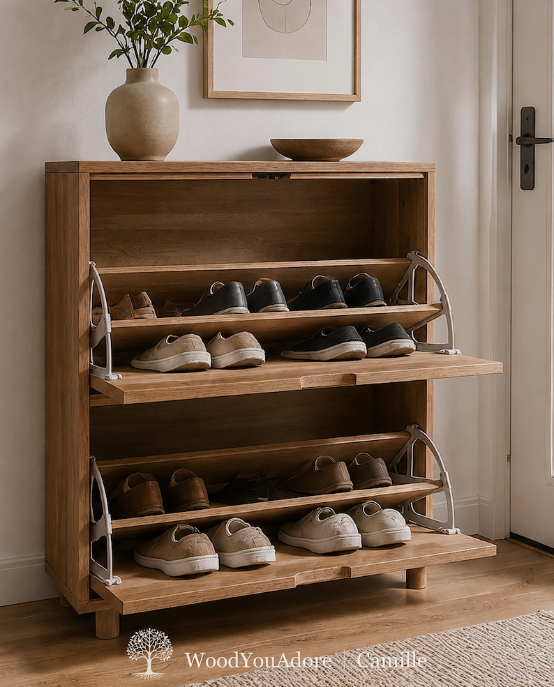 Op de afbeelding: Een schoenenkast van licht eikenhout met twee neerklapbare opbergvakken met metalen scharnieren. De kast bevat meerdere paren vrijetijdsschoenen op de planken. De tekst WoodYouAdore Camille staat onderaan in de afbeelding gedrukt.