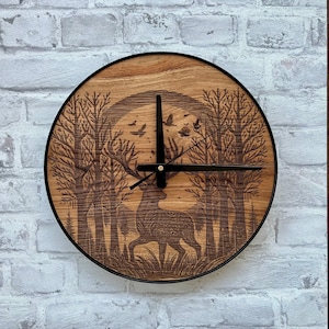 Könnte beinhalten: Runde Wanduhr aus Holz mit schwarzem Metallrahmen. Das Zifferblatt zeigt ein detailliertes Laser-Design eines Hirsches in einem Wald mit Vögeln. Die Zeiger der Uhr sind schwarz.