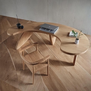 Peut inclure: Un bureau en bois clair avec un design incurvé unique, associé à une chaise assortie. Un ordinateur portable, une petite plante et des objets décoratifs sont sur le bureau. L'ensemble est posé sur un parquet.