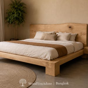 May include: A light-coloured wooden bed frame with a natural live-edge headboard featuring a visible knot and joinery details. The bed is dressed with white linens, a brown runner, and several pillows. Text reads: WoodYouAdore | Bangkok.