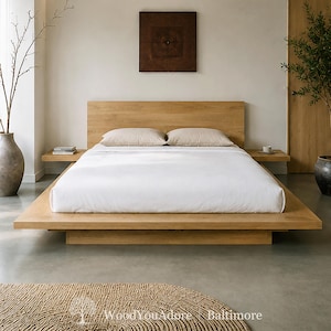 May include: A low-profile platform bed frame crafted from light-toned wood, featuring an integrated headboard and two attached floating side tables. The bed is dressed with a crisp white duvet and two beige pillows, creating a clean, horizontal aesthetic.