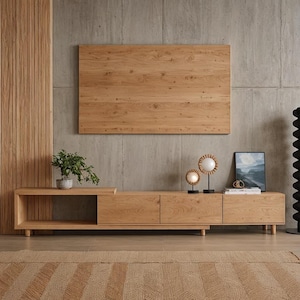 Peut inclure: Un meuble TV moderne en bois clair avec un panneau mural assorti. L'unité comprend des étagères ouvertes, des tiroirs et un placard fermé. Une petite plante en pot et des lampes décoratives sont posées sur le dessus.