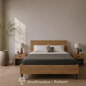 Könnte beinhalten: Ein hellbrauner Holzbettrahmen mit einer dunkelgrauen Bettdecke, zwei weißen Kissen und einem kleinen grauen quadratischen Kissen. Zwei passende Nachttische aus Holz mit Lampen flankieren das Bett. Eine große Topfpflanze steht links. Text WoodYouAdore Budapest.