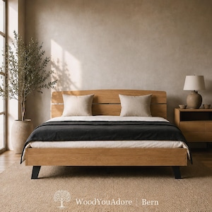 May include: A light-toned wooden bed frame with a curved headboard featuring horizontal slats. The bed is dressed with a white sheet, a dark charcoal grey blanket, and two beige square pillows. The frame is supported by four black legs.