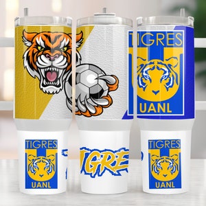 May include: Three white stainless steel tumblers with a blue, yellow, and orange tiger logo. The logo says "Tigres UANL". One tumbler has a tiger paw holding a soccer ball.