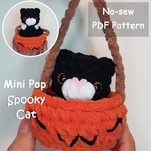 May include: A handmade, no-sew, plush black cat with a white muzzle and pink nose sits in an orange pumpkin basket. The basket has a brown handle. The text "Mini Pop Spooky Cat" and "No-sew PDF Pattern" are visible.