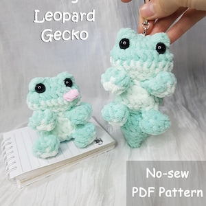 Puede incluir: Dos peluches de rana y gecko de ganchillo en tonos verde menta y blanco. Uno es sostenido por una mano, el otro está sobre un bloc de notas. La imagen incluye el texto "Frog Leopard Gecko" y "No-sew PDF Pattern".