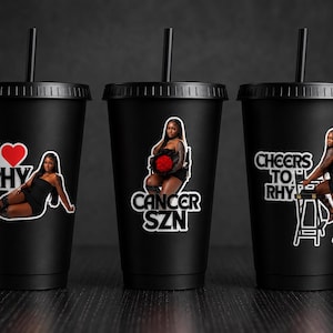 May include: Three matte black reusable plastic tumblers with lids and straws. Each cup features a different graphic decal: one says I heart RHY with a person, one says CANCER SZN with a person holding red roses, and one says CHEERS TO RHY with a person.