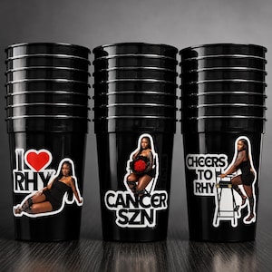 May include: Three stacks of black plastic cups featuring custom decals. The first cup shows a red heart, the text I LOVE RHY, and a person in a black dress. The second shows CANCER SZN and a person with red roses. The third shows CHEERS TO RHY.
