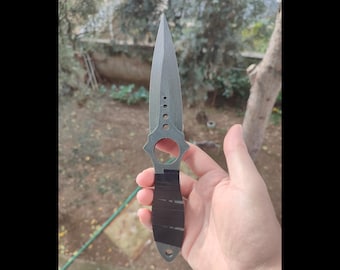 May include: A grey and black throwing knife with a ring handle. The knife has a black tape handle and a grey blade with a pointed tip.