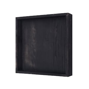 May include: A square, black wooden tray with a recessed interior. The tray is made of dark wood with visible grain and a matte finish. The sides are approximately 2 inches high, creating a shallow container.