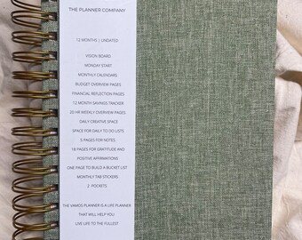 May include: A green planner with a gold spiral binding. The cover has a textured fabric design. The front cover has a white label with the text "VAMOS THE PLANNER COMPANY" and a list of features, including 12 months undated, vision board, monthly calendars, budget overview pages, financial reflection pages, 12 month savings tracker, 20 hr weekly overview pages, daily creative space, space for daily to do lists, 5 pages for notes, 18 pages for gratitude and positive affirmations, one page to build a bucket list, monthly tab stickers, 2 pockets, The VAMOS planner is a life planner that will help you live life to the fullest, Thank you for joining our family.