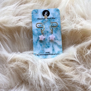 May include: A pair of pink star-shaped earrings with gold hoops. The earrings are on a card that says "Elizabeth's Nook Shop" and includes an email address.