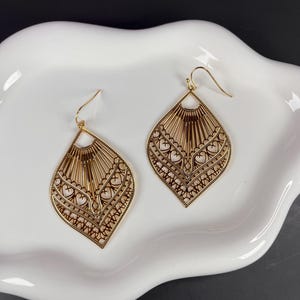 May include: A pair of gold filigree earrings with a teardrop shape and intricate heart designs.