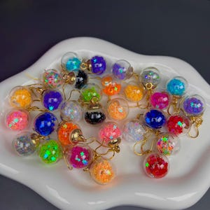 May include: A collection of colorful glass earrings with gold hooks. Each earring contains a variety of star-shaped glitter.
