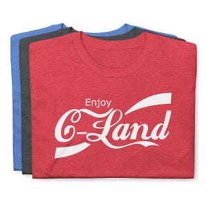 Pode incluir: Camiseta vermelha, cinza e azul com o texto "Enjoy C-Land" em uma fonte branca estilizada.