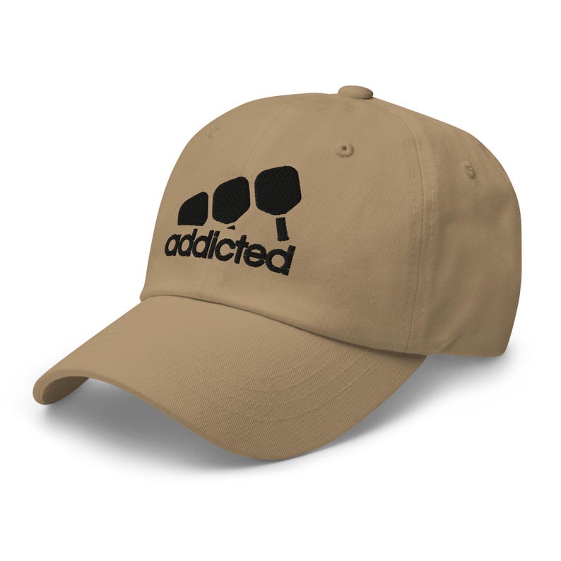 May include: A tan baseball cap with black embroidery of three paddleball paddles and the word "addicted".