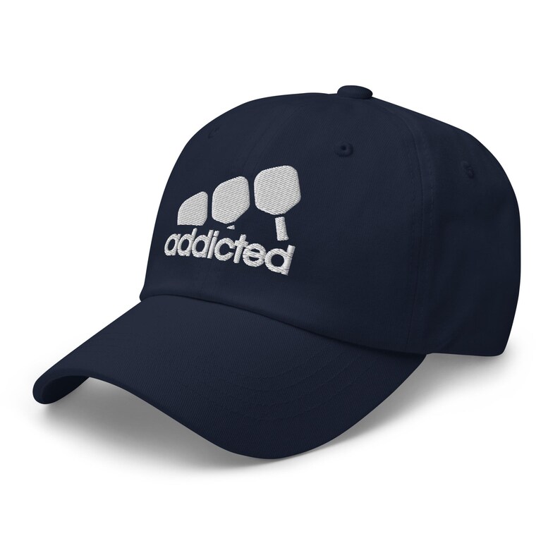 May include: A navy blue baseball cap with white embroidery of three paddleball paddles and the word "addicted".