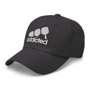 May include: A black baseball cap with a white embroidered design of three paddleball paddles and the word "addicted".