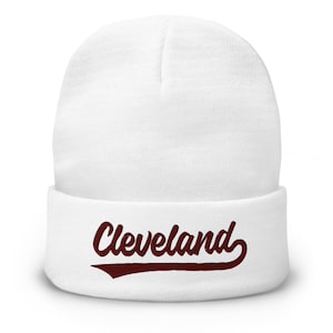 May include: A white beanie with the word "Cleveland" in a maroon script font across the folded brim. The beanie is made of a soft, knitted material.