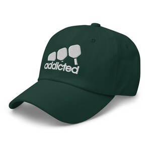 May include: A dark green baseball cap with a white embroidered design of three pickleball paddles and the word "addicted".