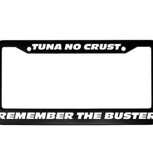 May include: Black metal license plate frame with white text that reads "TUNA NO CRUST. REMEMBER THE BUSTER."
