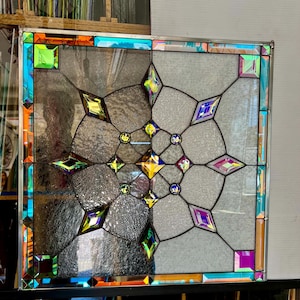 May include: A stained glass window panel with a geometric design featuring a central starburst surrounded by diamond shapes. The glass is iridescent and features shades of blue, green, purple, and gold.