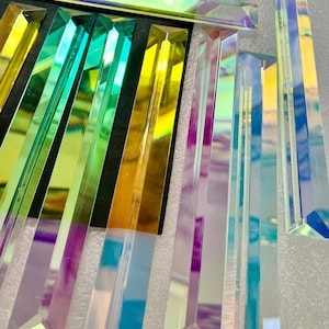 May include: An array of iridescent glass prisms in various sizes. The prisms reflect a spectrum of colors, including yellow, green, and purple. Some prisms are arranged on a black surface, while others stand upright.