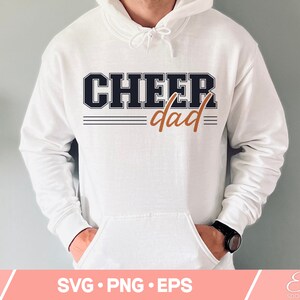 May include: White hoodie with the text "CHEER dad" in black and orange lettering. The text is in a varsity style font.
