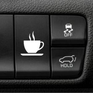 May include: A black plastic vehicle dashboard button featuring a white graphic of a steaming coffee cup on a saucer. To the right are two smaller buttons with white icons: one showing a car with wavy lines and the text OFF, and one showing a car with an open trunk and the text HOLD.