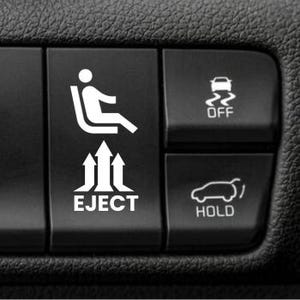 May include: A black rectangular car interior button featuring a white graphic of a person sitting in a seat with three upward-pointing arrows underneath and the word EJECT printed below. To the right are two smaller buttons with vehicle icons.