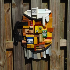 May include: A wooden beer stein made from various pieces of wood, including a Bud Light can, a Heineken can, and a red can. The stein is mounted on a wooden fence.