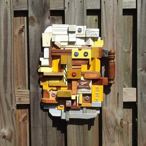May include: A colorful mosaic artwork made from wood scraps and bottle caps. The artwork features a Miller High Life beer logo and is mounted on a wooden fence.