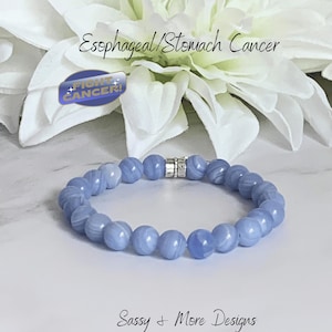 May include: A light blue beaded bracelet with a silver clasp. The bracelet is in front of a white flower and a blue and white sticker that says "FIGHT CANCER!". The text "Esophageal/Stomach Cancer" is above the bracelet.