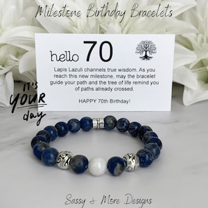 May include: A lapis lazuli bracelet with silver accents and a white bead. A card reads "hello 70" with the text "Happy 70th Birthday!" and "Milestone Birthday Bracelets". The bracelet is on a white surface.