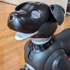 May include: A black robotic dog with a white mouth and a decorative collar. The dog has large, expressive eyes and a sleek, modern design. The dog is made of plastic and has a smooth, glossy finish.