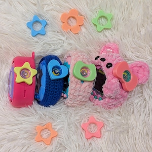May include: A collection of colorful toy watches and accessories. The watches are pink, blue, and pink, with star and heart-shaped details. Additional star and flower-shaped accessories in blue, orange, and green are scattered around.
