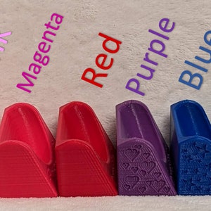 May include: A range of 3D-printed shoe heel protectors in colours such as white, yellow, pink, magenta, red, purple, blue, light blue, green, and black. Each protector has a unique design and is labelled with its colour.
