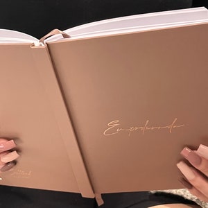 Puede incluir: Un diario encuadernado en cuero marrón claro con la palabra "Empowered" escrita en letras doradas en la portada.