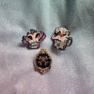 May include: Three enamel pins featuring a skull-like robot, a white robot with a green eye, and a gold key symbol on a blue background.