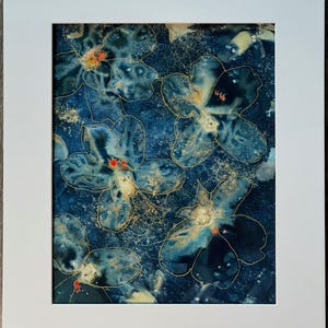 May include: Abstract floral art print featuring blue and gold flowers on a dark blue background. The artwork is framed in a white mat. The flowers have gold outlines and red accents, creating a striking contrast.