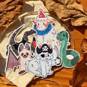 May include: A set of five colorful animal stickers featuring a black and white bat, a black and white lizard, a white sheep wearing a blue and white collar, a white dog wearing a pirate hat and eye patch, and a green snake.