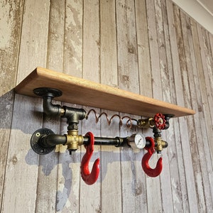 May include: A wooden shelf with black pipe fittings and red hooks. The shelf is mounted to a wood-panelled wall. The pipe fittings have a gauge and a valve.