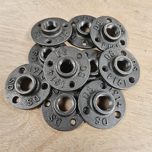 Peut inclure: Un ensemble de brides de tuyauterie circulaires en métal gris foncé, chacune dotée d'un trou central fileté entouré de quatre petits trous de montage. La surface de chaque bride porte l'inscription DS et 1914 en relief.